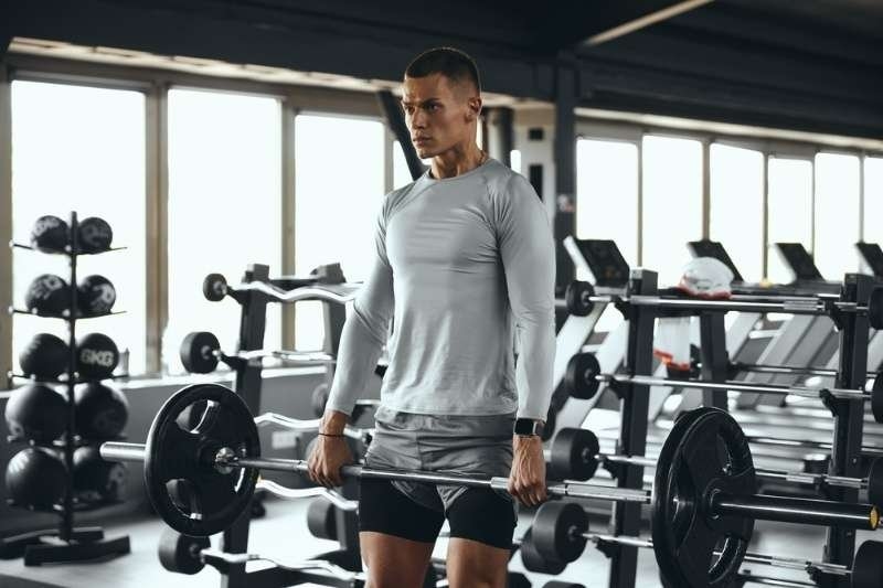A man performing a barbell exercise in a gym surrounded by weights and fitness equipment.