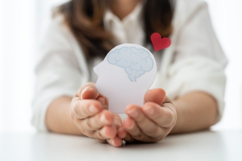 Person holding a paper cutout of a human head with a brain illustration and a red heart symbol.