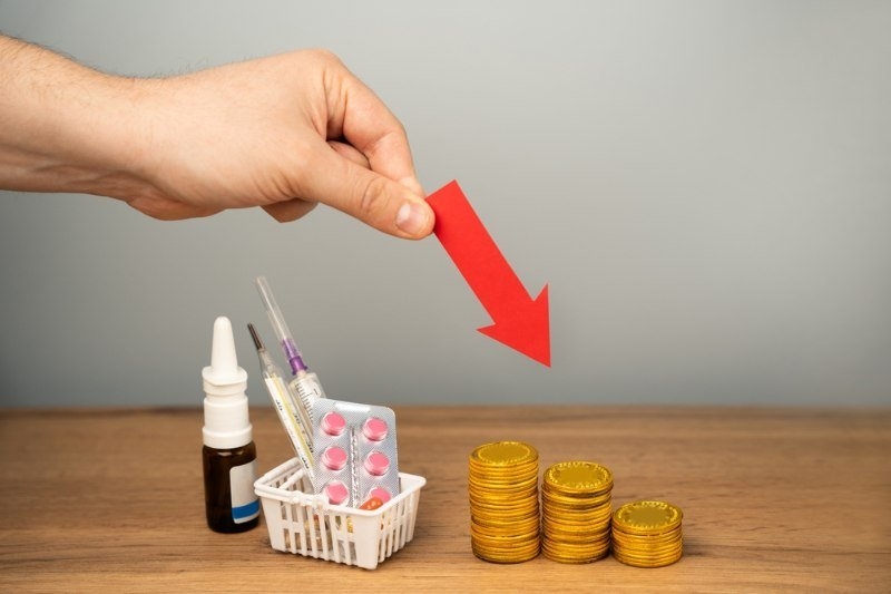 Down arrow, coins and basket with medical pills. Concept of reducing the price of medicines and drugs.