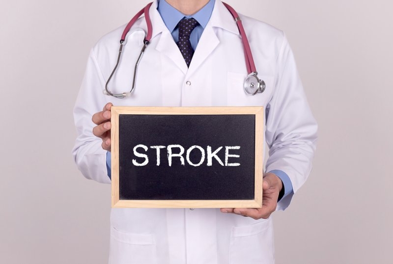 Doctor holding a chalkboard with the word “STROKE” displayed prominently.