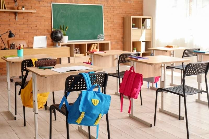 Empty classroom with desks, chairs, backpacks, and a chalkboard, representing a school learning environment.