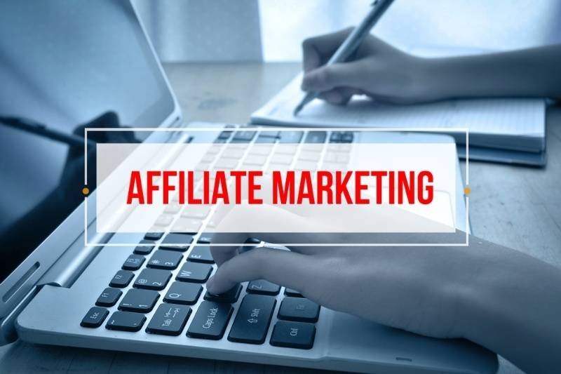 A laptop and hands working at a desk are shown with a prominent overlay reading “AFFILIATE MARKETING.”
