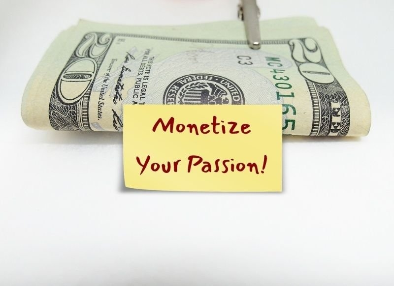 A rolled U.S. $20 bill is positioned behind a yellow sticky note that reads “Monetize Your Passion!” on a white background.