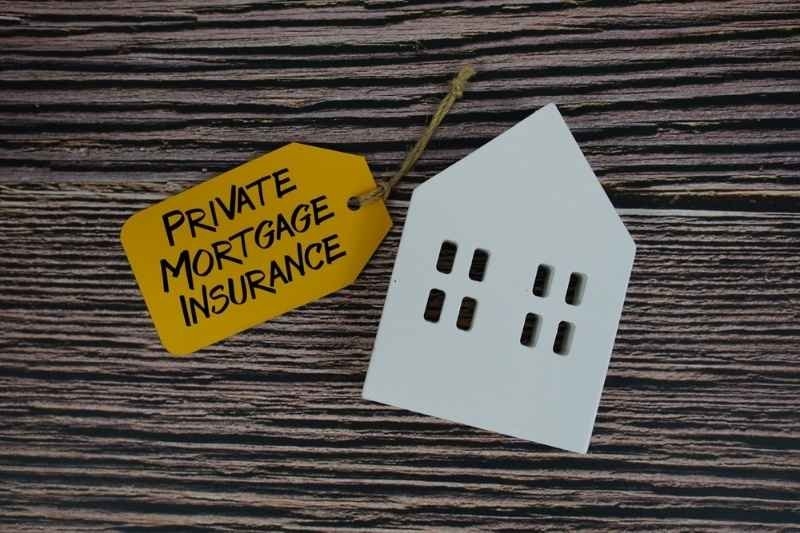 Paper house cutout beside a tag labeled “Private Mortgage Insurance” on a wooden surface, illustrating PMI coverage for home loans.