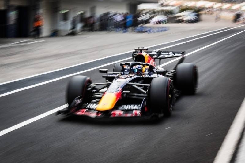 A Formula-style race car speeds along a pit lane or racetrack, captured with motion blur to emphasize its high speed.