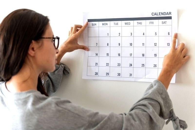 A woman adjusting a monthly calendar on a wall.