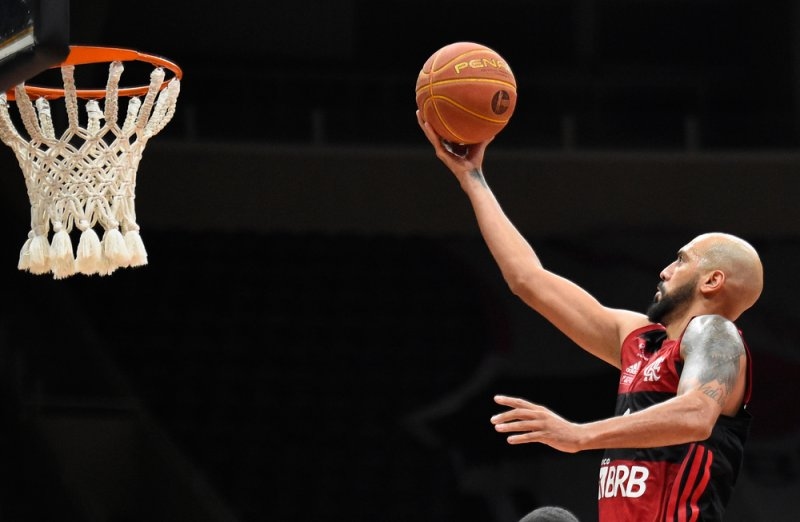 Basketball player in a red and black jersey attempting a one-handed shot toward the hoop on an indoor basketball court.