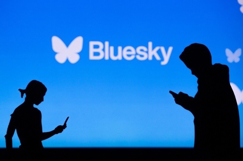 Silhouettes of two people using smartphones appear in front of a blue background featuring the Bluesky logo and name.
