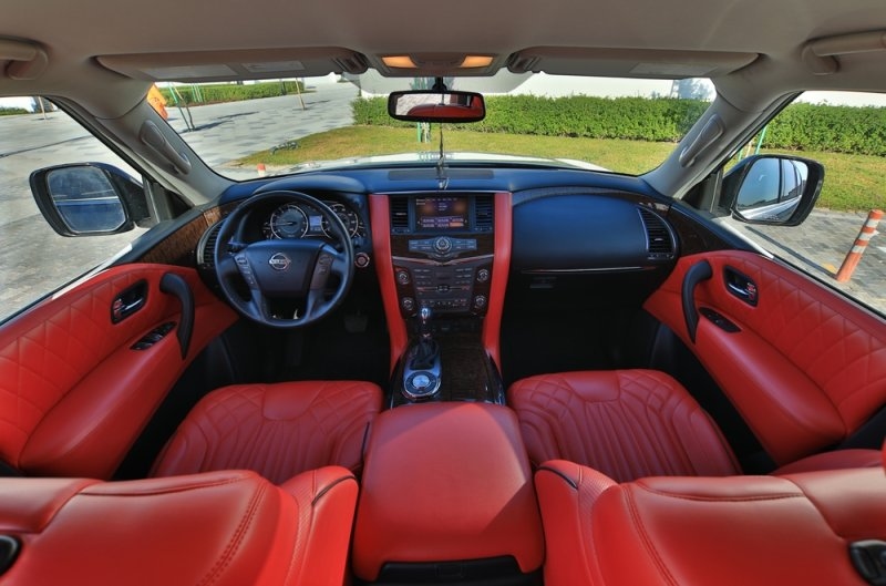 Luxury Nissan SUV interior featuring red leather seats, a dashboard-mounted infotainment system, and wood-trim accents.