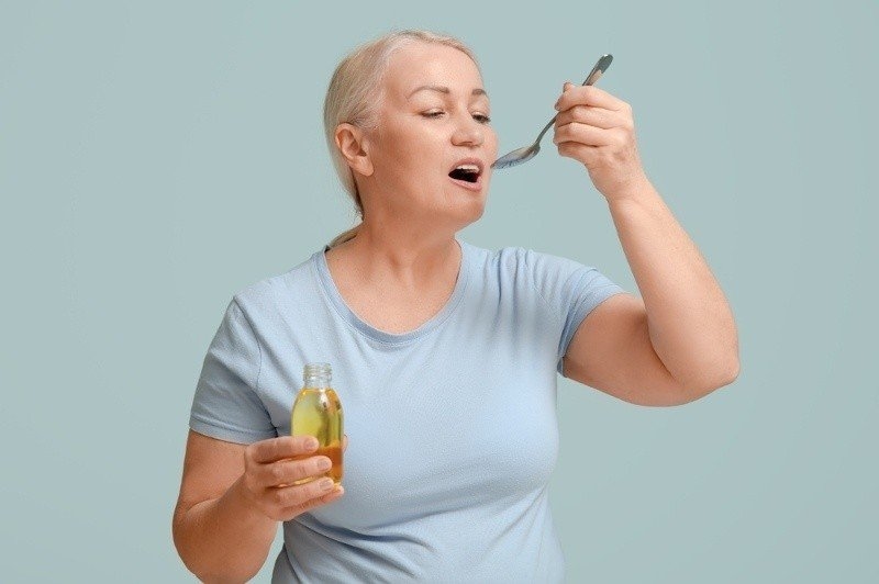 Older woman taking a spoonful of liquid supplement.
