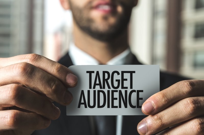 A businessman holds a card labeled “Target Audience,” representing customer targeting and market segmentation.