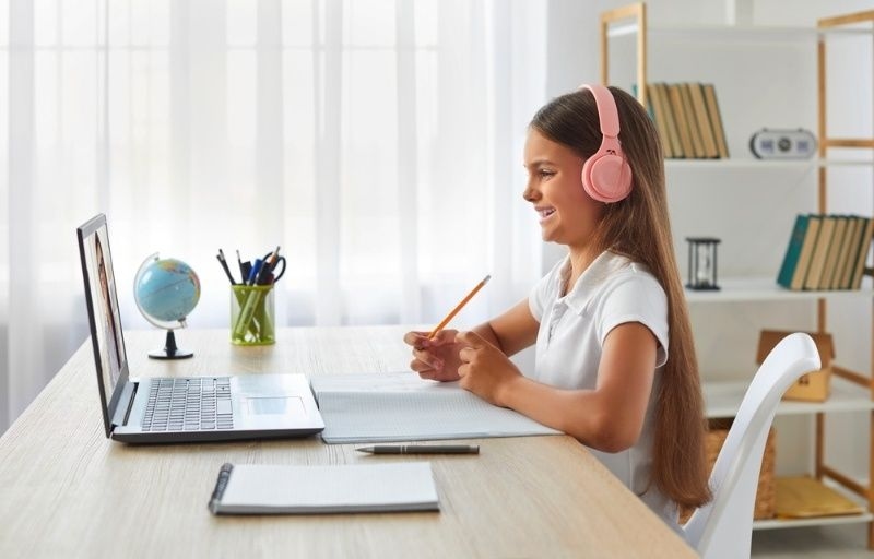 Young girl wearing pink headphones while studying during an online learning session on a laptop.