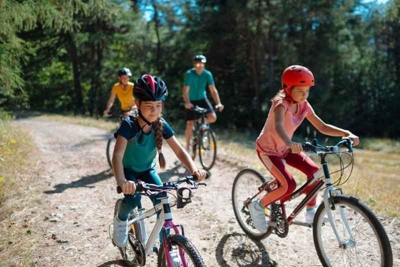 Children and adults riding bicycles together on a forest trail, enjoying an outdoor family cycling activity in nature.