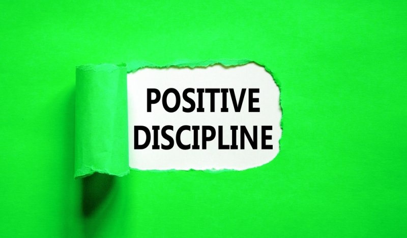 Paper sign reading “POSITIVE DISCIPLINE” against a bright green background.
