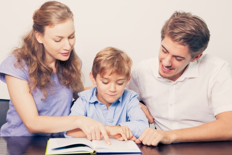 Smiling Mother and Father Teaching Son to Read
