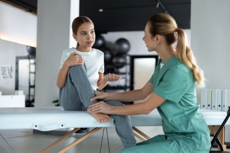 Physical therapist evaluating a young girl's knee and leg during a pediatric rehabilitation or physiotherapy session.