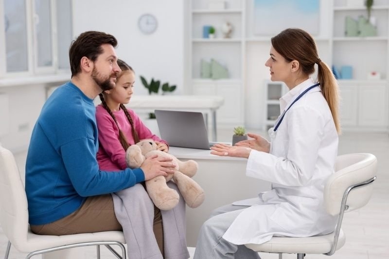Pediatrician consulting with a father and young daughter during a medical appointment in a healthcare clinic.