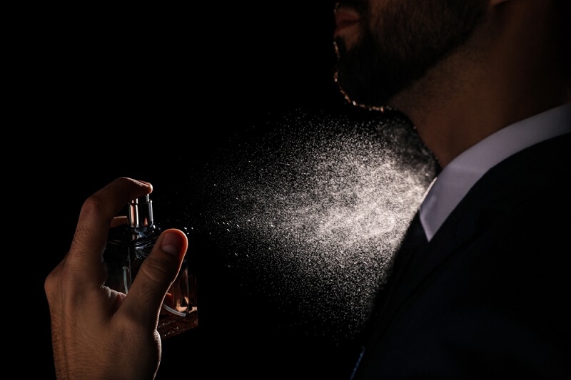 man spraying perfume on his nech 