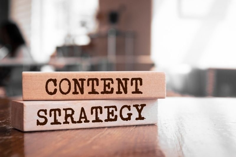 Two wooden blocks stacked on a desk are labeled “CONTENT” and “STRATEGY.”