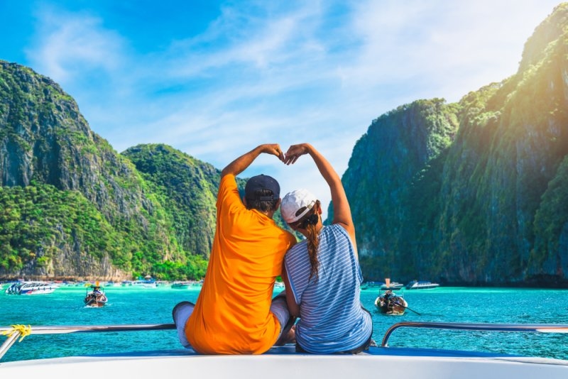 Couple forming a heart shape with their arms while viewing a tropical bay from a boat.