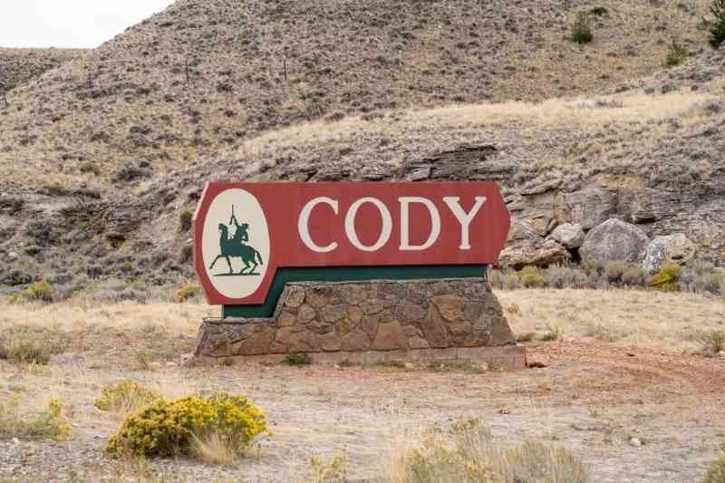 A red roadside sign reading “CODY” with a cowboy silhouette stands against a dry, mountainous landscape.