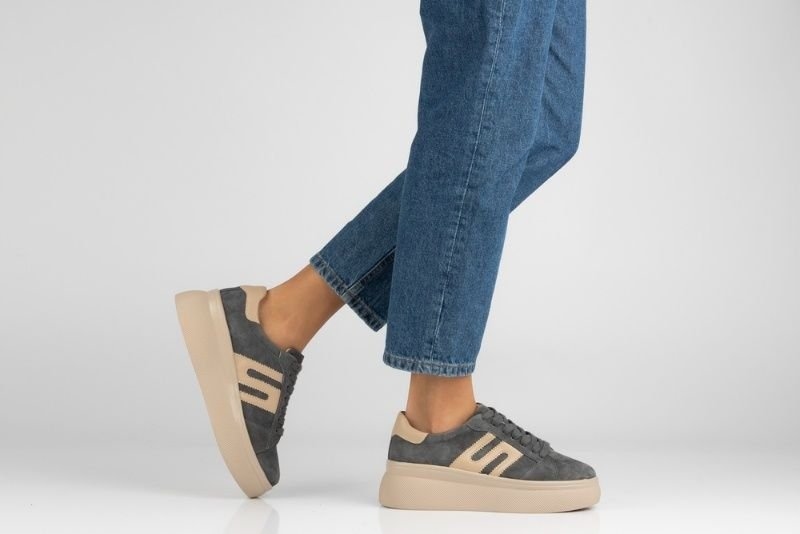 Stylish women's grey suede platform sneakers with beige accents and thick soles paired with blue jeans.