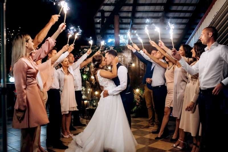 Bride and groom kissing while guests hold sparklers around them during a nighttime wedding celebration.