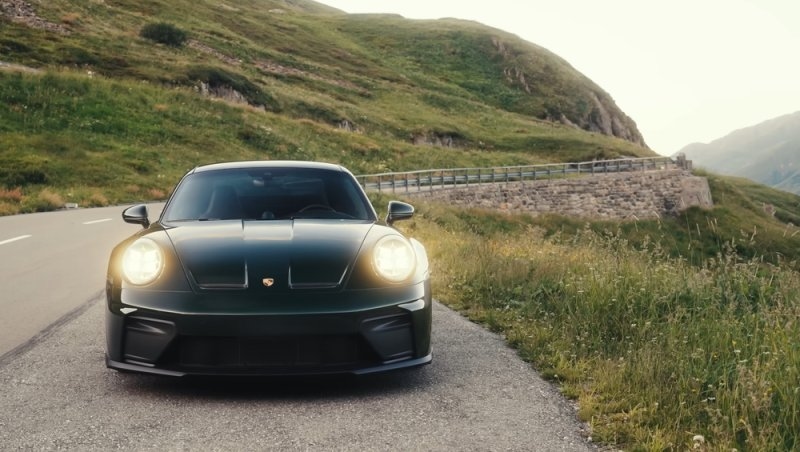 Black Porsche 911 sports car parked on a winding mountain road surrounded by green hills.