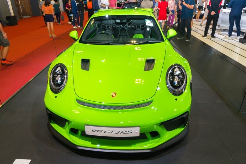 Bright green Porsche 911 GT3 RS displayed at an indoor auto exhibition with visitors in the background.