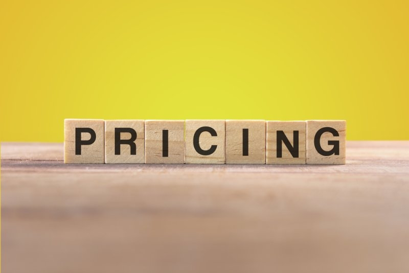 Wooden letter blocks spelling “PRICING” on a table against a yellow background.