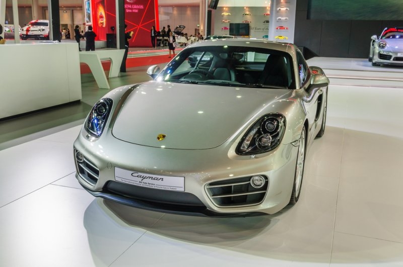 Silver Porsche Cayman sports car displayed at an indoor automotive exhibition.