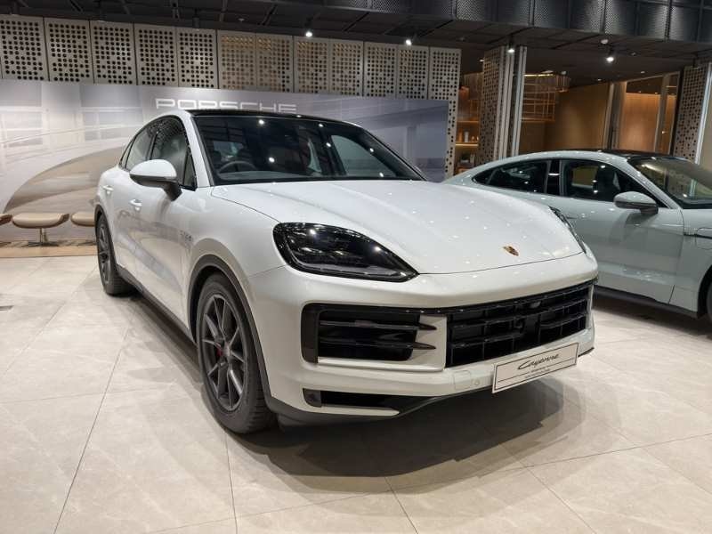A white Porsche Cayenne displayed inside a showroom, photographed from the front three-quarter angle.