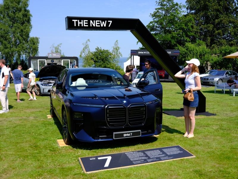 Dark blue BMW 7 Series displayed at an outdoor automotive event beneath a sign reading “THE NEW 7.”