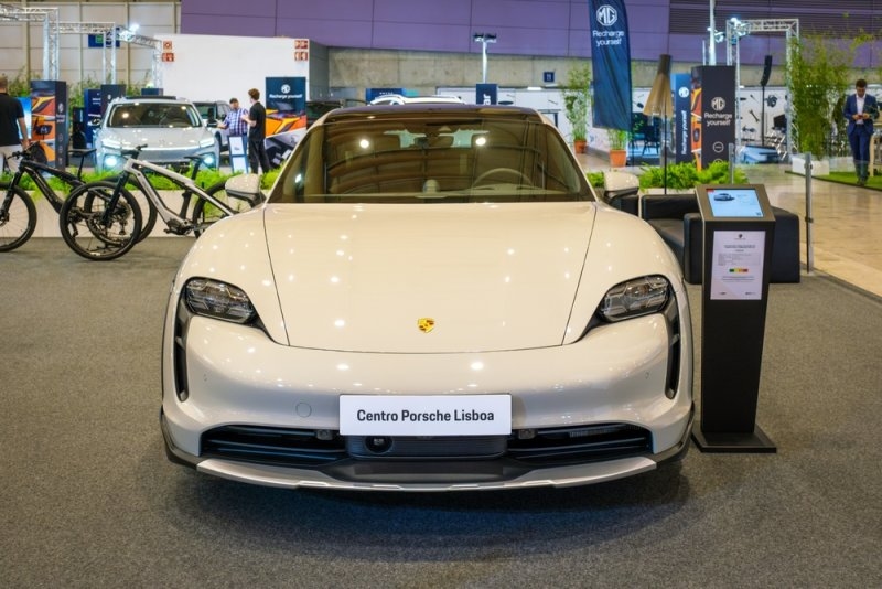 A white Porsche Taycan displayed at an indoor automotive exhibition.
