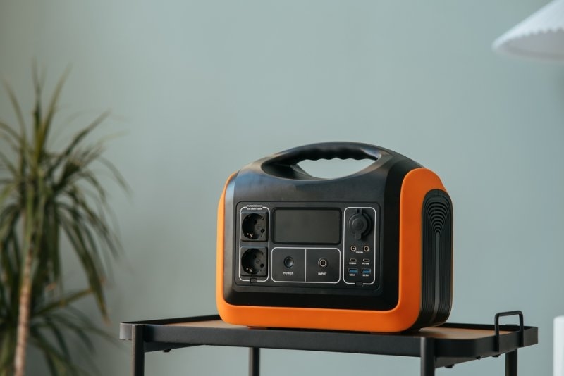 Black and orange portable power station with multiple outlets and ports displayed on a table indoors.