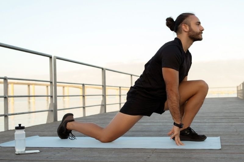 Athlete performing a kneeling hip flexor stretch outdoors on a yoga mat to improve flexibility and mobility.