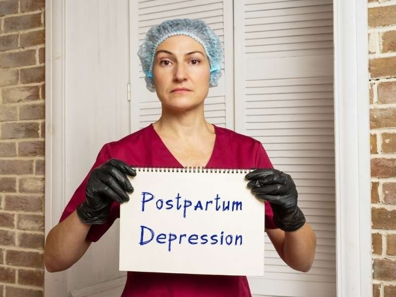 Healthcare professional holding a sign that reads "Postpartum Depression" to raise awareness about maternal mental health.