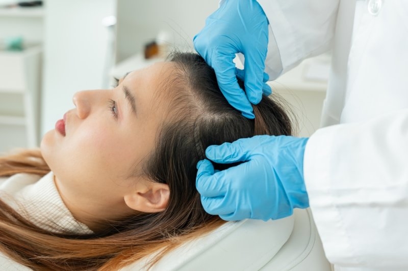Dermatologist examining a woman's scalp for hair thinning.