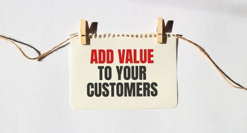 ADD VALUE TO YOUR CUSTOMERS text words inscription on yellow sticker note on white wall or table.