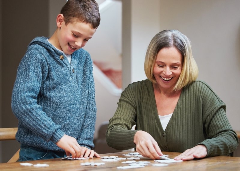 Mother and young boy working together on a jigsaw puzzle at a table.