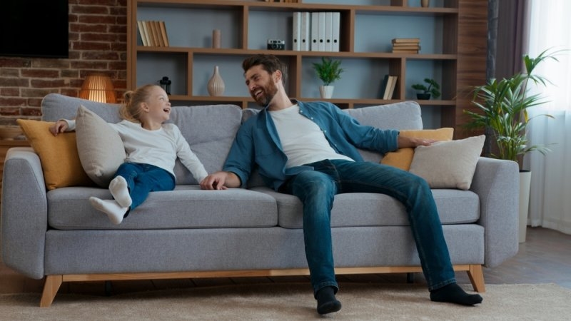 Father and daughter smiling and relaxing together on a sofa at home.