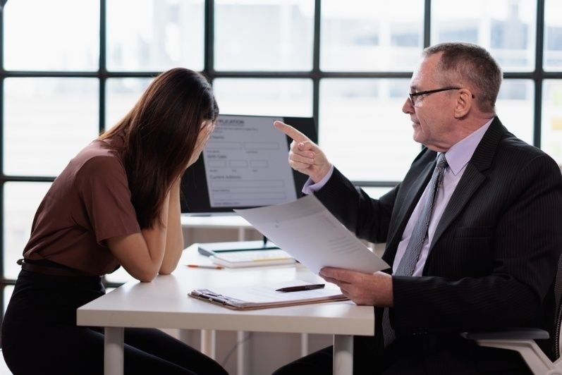 Business manager pointing at a distressed employee during a disciplinary meeting.