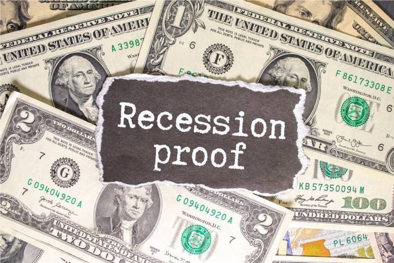 U.S. dollar bills surrounding a sign labeled “Recession Proo.”