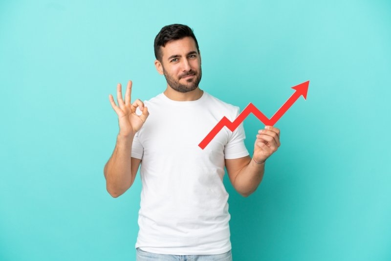 A smiling man holds a red upward-trending arrow.