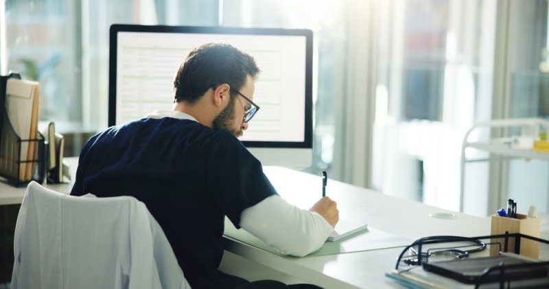 Employee working at a desk with a computer and paperwork in a professional office setting.