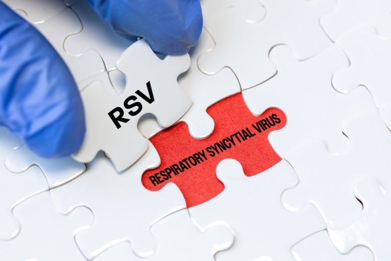 Close-up of gloved hands fitting a puzzle piece labeled “RSV” into a puzzle showing “Respiratory Syncytial Virus.”