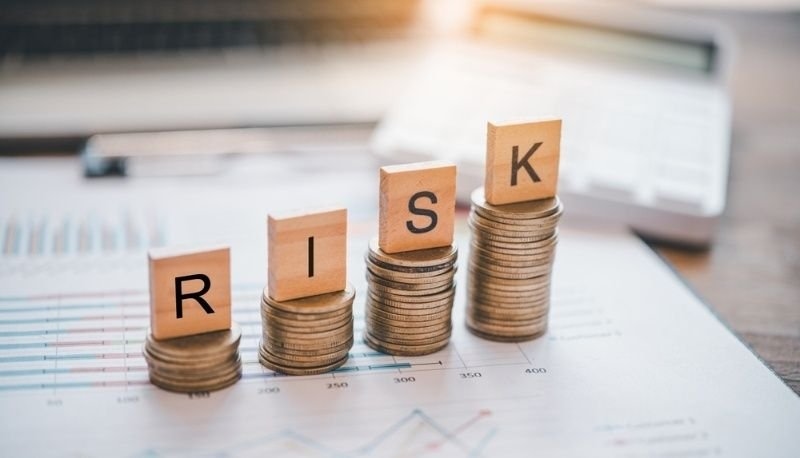 Wooden letter blocks spelling "RISK" stacked on columns of coins.
