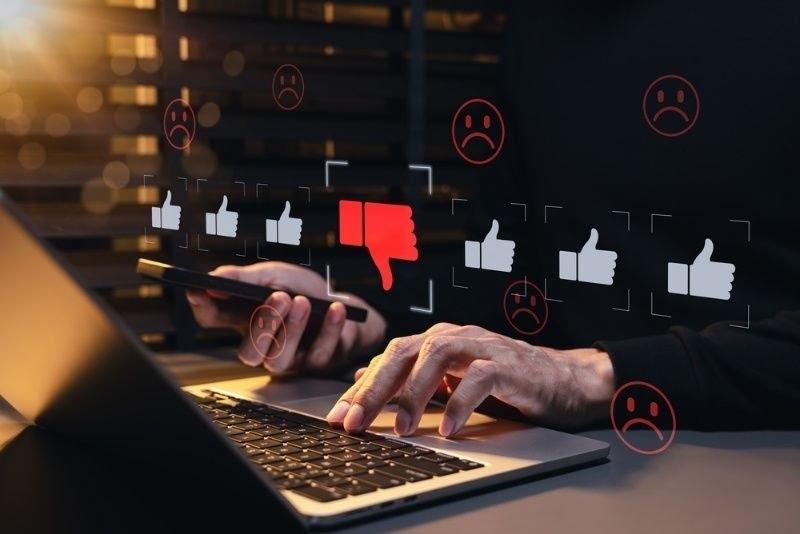 Person using a laptop and smartphone with a digital interface showing thumbs-down icons, negative ratings, and unhappy feedback.