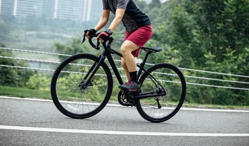 Cyclist riding a road bike on a paved path through a green park, representing fitness, cycling, and outdoor exercise.