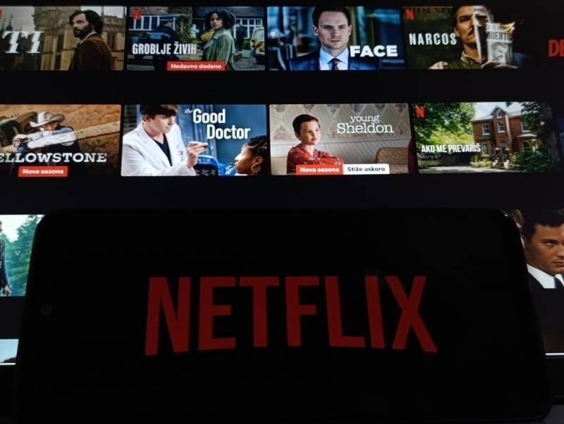 Netflix logo displayed on a smartphone screen with various TV show and movie thumbnails in the background.